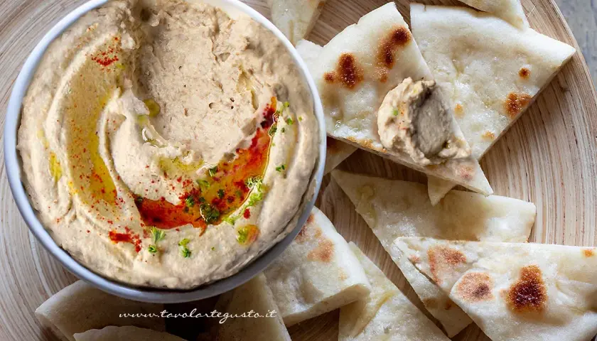 Ciotola di hummus di lenticchie con olio, paprika e prezzemolo, servito con pane pita tagliato a spicchi.