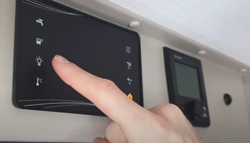 Doigt appuyant sur l'icône d'ampoule du tableau de commande cellule camping-car Challenger.