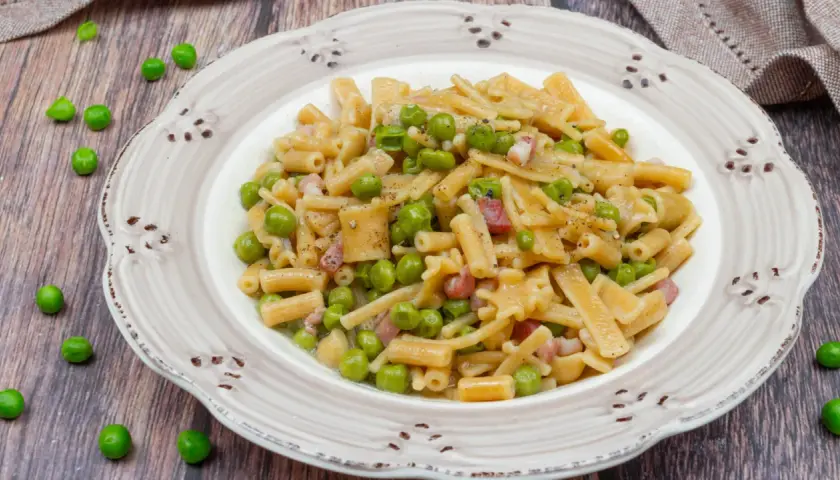 Un piatto di pasta con piselli, pancetta e pepe nero, servito su un piatto rustico.