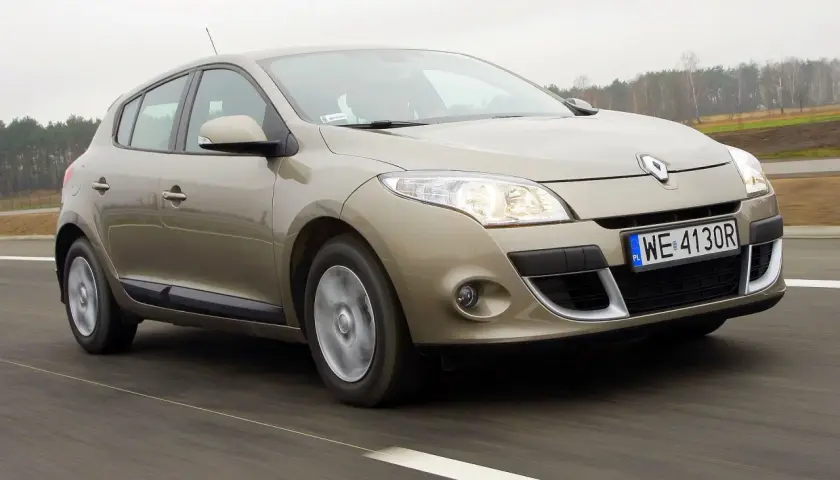 Złoty Megane 3 w ruchu drogowym, z widocznymi światłami i tablicą rejestracyjną WE 4130R.