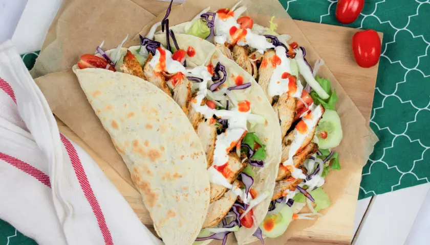 Kebab w tortilli z kurczakiem, warzywami i sosami, obok pomidorki.