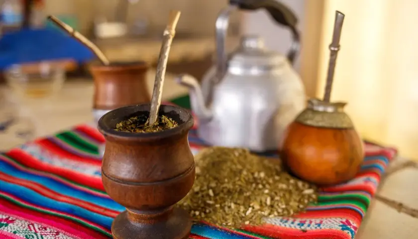 Tradycyjny rytuał z yaguar yerba mate: drewniane naczynia, bombille i czajnik na kolorowym obrusie.