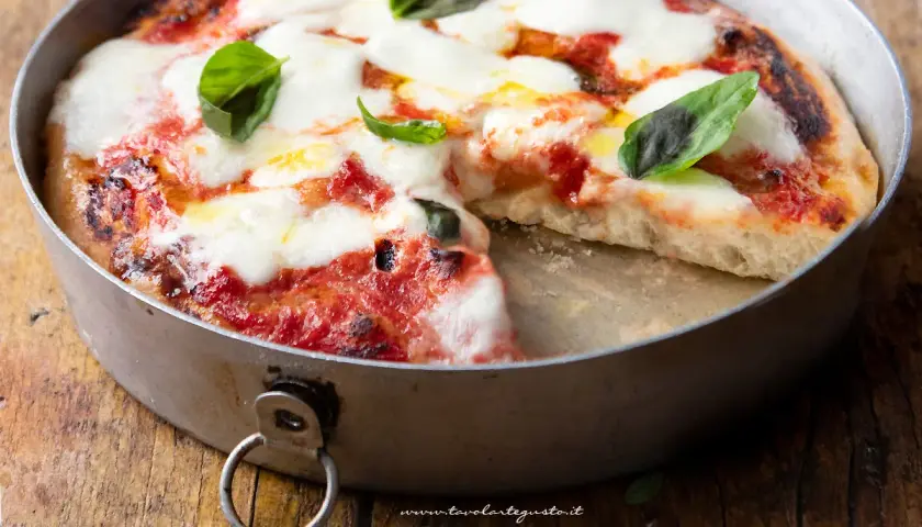 Pizza margherita appena sfornata in friggitrice ad aria, con mozzarella filante e basilico fresco su un tagliere di legno.