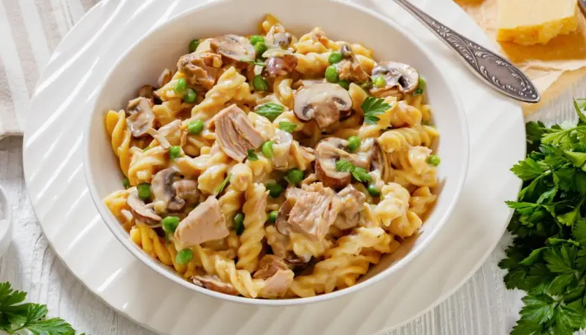 Makaron fusilli z tuńczykiem, groszkiem i pieczarkami w kremowym sosie, udekorowany natką pietruszki.