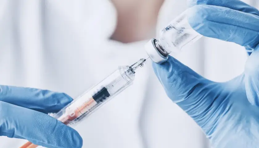 Ręce w niebieskich rękawiczkach pobierają płyn z fiolki do strzykawki. To może być propofol, środek znieczulający.