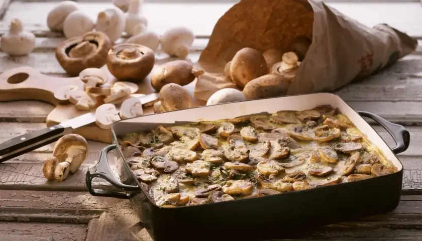 Frisch zubereiteter low carb champignon-auflauf in einer Auflaufform, umgeben von frischen Champignons.