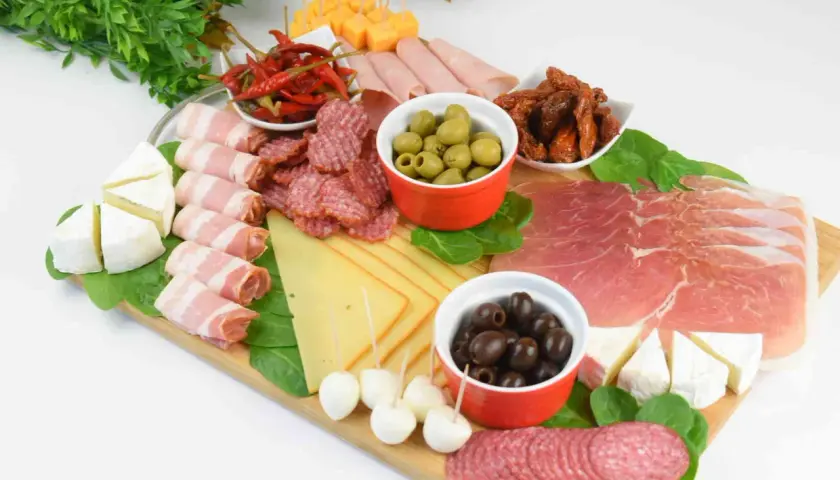 Patera wędlin i serów: salami, szynka, prosciutto, sery, oliwki, suszone pomidory i papryczki chili.