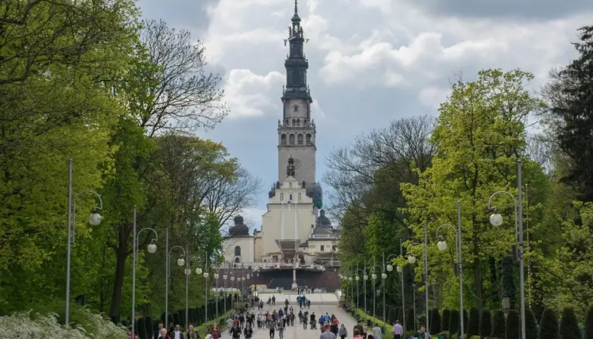 Aleja prowadząca do Jasnej Góry, jednego z najważniejszych sanktuariów maryjnych w Polsce. Ludzie spacerują w kierunku imponującej wieży klasztornej.