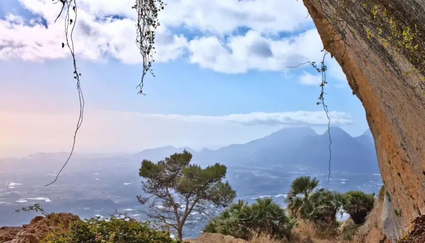 Vista desde el Forat de Bernia, con vegetación colgante y un paisaje montañoso al fondo.