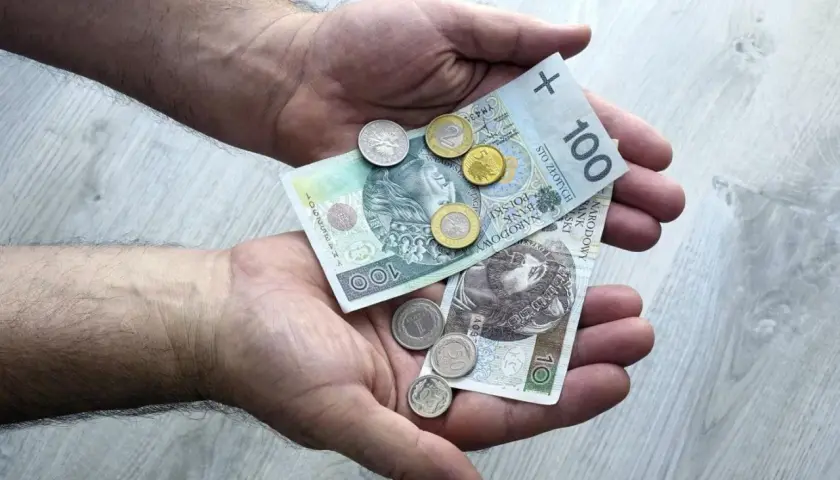 Dłonie trzymające polskie banknoty 100 zł i monety.