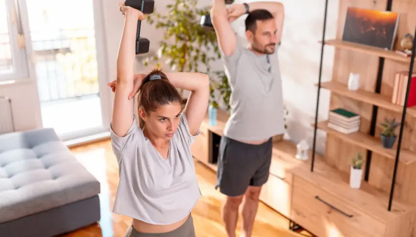 Para ćwiczy ćwiczenia na triceps w domu, podnosząc hantle nad głowę.