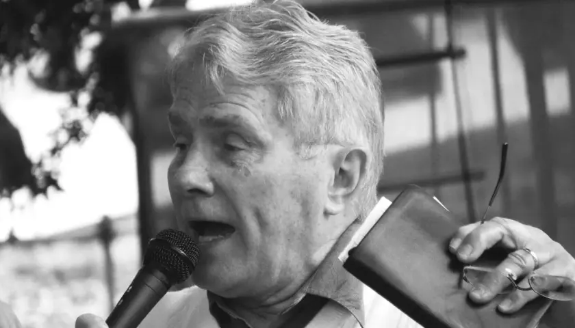 Luis Palau spricht ins Mikrofon, hält eine Bibel und eine Brille.