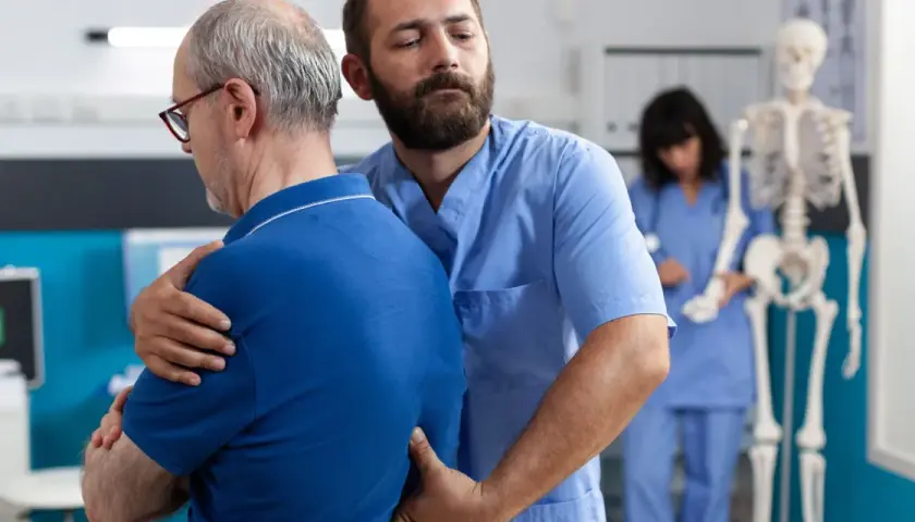 Fizjoterapeuta pomaga pacjentowi z bólem pleców i mięśni. W tle szkielet i pielęgniarka.