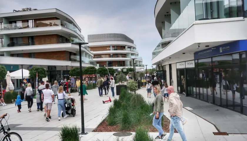 Spacer po nowoczesnej promenadzie w Świnoujściu, gdzie liczne atrakcje czekają na turystów. Ludzie spacerują, sklepy i apartamenty zachwycają architekturą.
