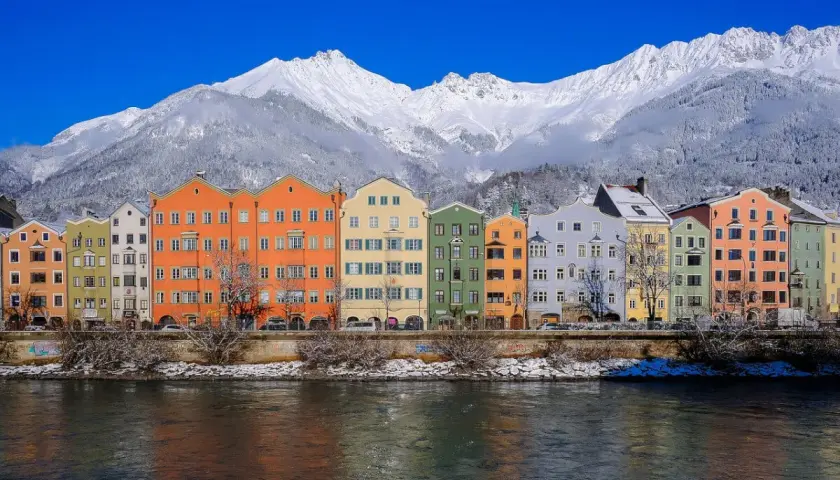 Kolorowe kamienice nad rzeką, w tle ośnieżone góry. To piękne Innsbruck atrakcje, które warto zobaczyć zimą.