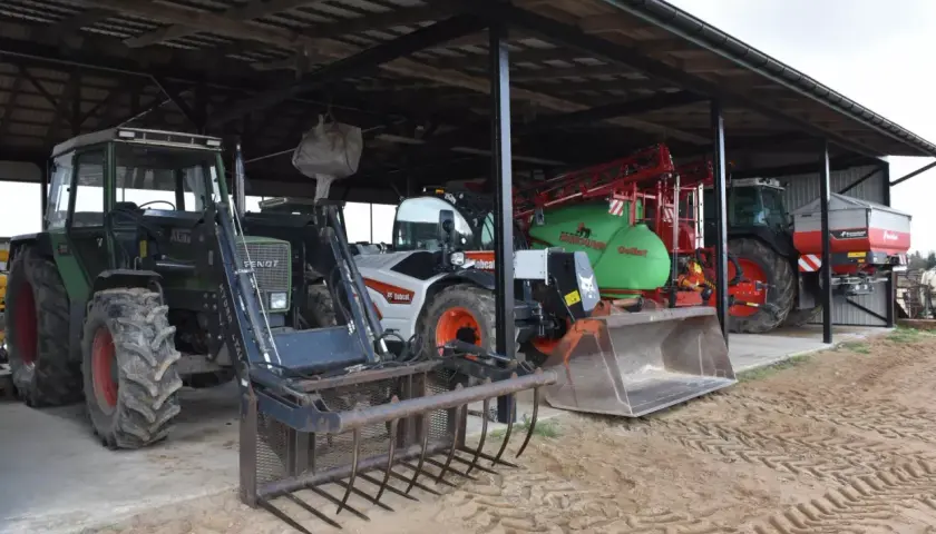 Ciągniki i maszyny rolnicze pod zadaszeniem. Widać zielony Fendt z ładowaczem, biały Bobcat, zielony opryskiwacz i ciągnik z rozsiewaczem. To wszystko w budynku gospodarczym bez zgłoszenia.