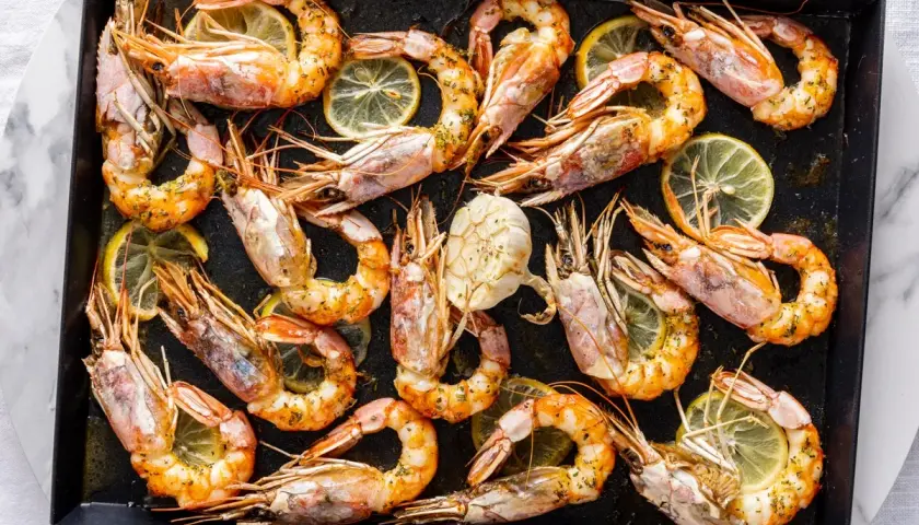 Gamberoni al forno dorati e succulenti, conditi con erbe aromatiche e fette di limone, pronti per essere gustati.