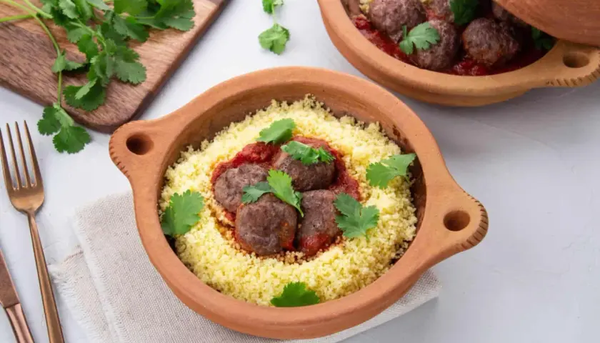 Délicieuse recette de boulette de boeuf haché avec sauce, servie sur un lit de couscous et garnie de coriandre fraîche.