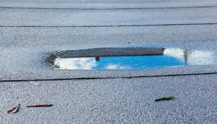 Pfützen auf Bitumenschindeln: Was tun bei undichten Stellen? Wasser sammelt sich auf dem Dach, ein Zeichen für mögliche Schäden.