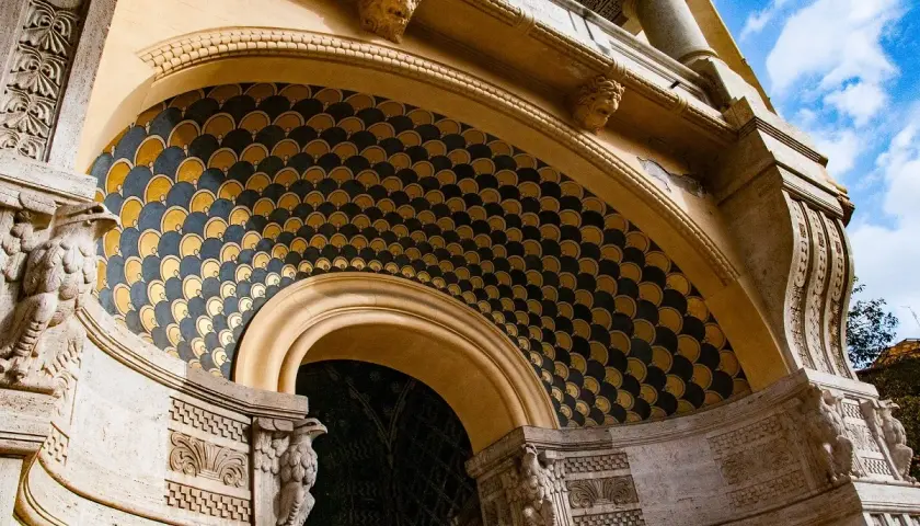 Dettaglio architettonico con decorazioni a squame dorate e blu, sculture di aquile e teste leonine. Un esempio di architettura del quartiere Coppedè.
