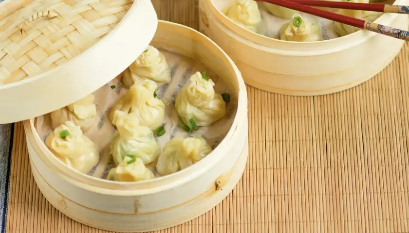 Parujące pierożki z ciasta do wontonów w bambusowych parownikach, ozdobione szczypiorkiem.