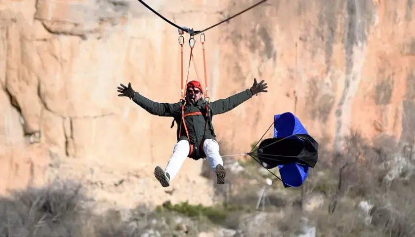 Hombre disfrutando de una tirolina de cuenca, con los brazos extendidos y una gran sonrisa, mientras desciende por un acantilado.