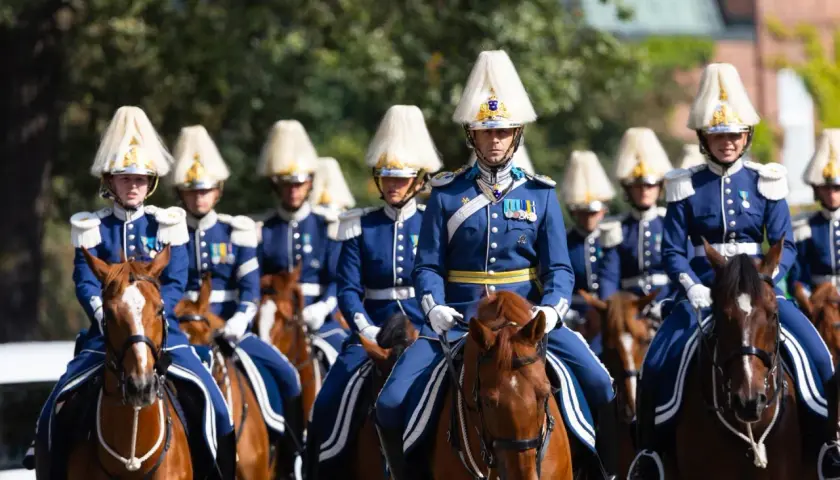 Livgardet i sina blå uniformer och höga hattar rider på bruna hästar.