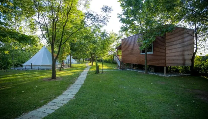 Glamping w Albanii, blisko morza jońskiego. Białe namioty i drewniany domek na wzgórzu, otoczone zielenią.