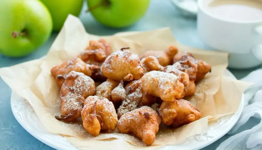 Montón de buñuelos de manzana dorados y espolvoreados con azúcar glas, listos para disfrutar.