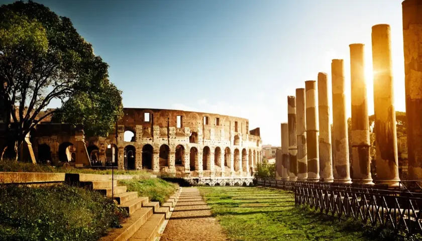 Colosseo illuminato dal sole, un'icona tra le cose da non perdere a Roma. Colonne antiche e un sentiero lastricato invitano alla scoperta.