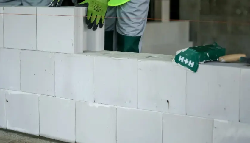 Budowa ściany z białych pustaków silikatowych. Ręce w zielonych rękawicach układają kolejny blok.