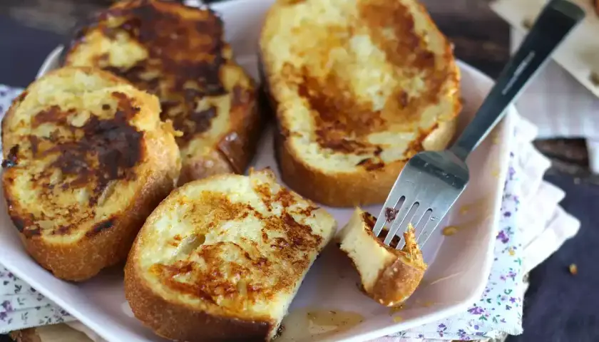 Un plat de pain perdu salé, doré et appétissant, avec une fourchette piquant un morceau. Un délice pour le petit-déjeuner ou le brunch.