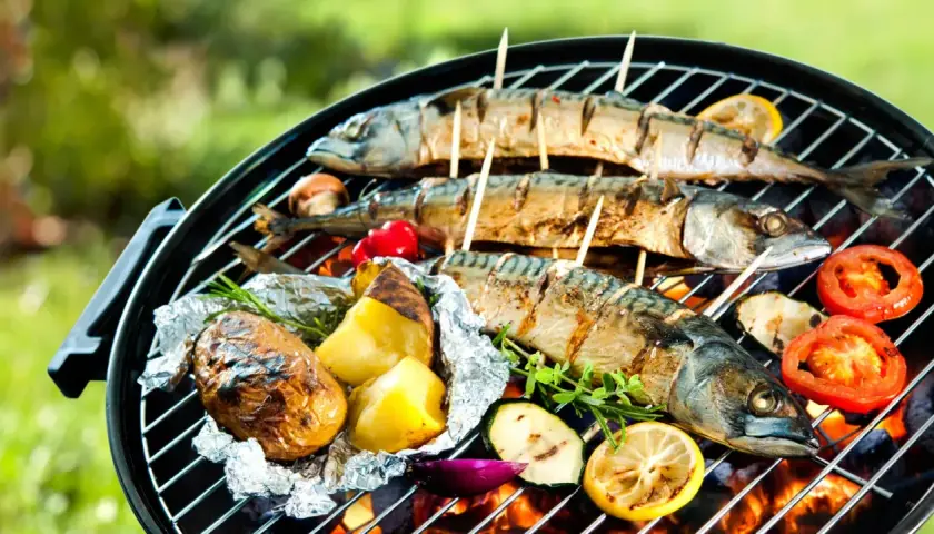 Trois poissons maquereaux grillés sur un barbecue, accompagnés de pommes de terre en papillote, de tomates et de citrons. Un délice de poisson barbecue en plein air.