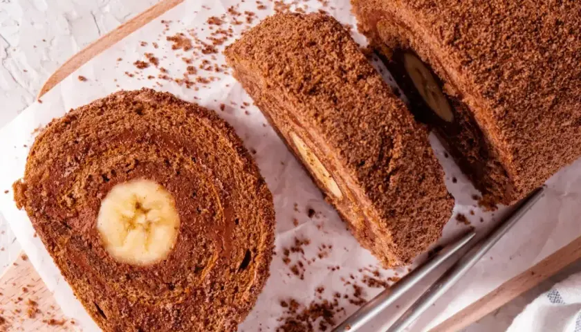 Czekoladowe ciasto gąbka z bananem w środku, pokrojone na plastry, posypane wiórkami.