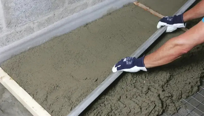 Ręce w rękawiczkach wyrównują świeży styrobeton lambda za pomocą łaty.