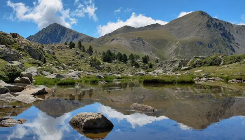 Reflejo de montañas y nubes en un lago sereno del valle de Madriu-Perafita-Claror.