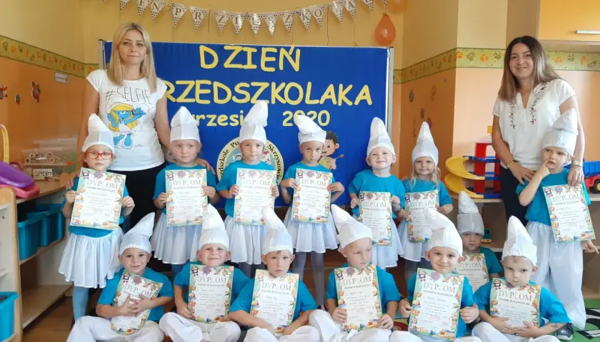 Dzieci w strojach smerfów z dyplomami, z nauczycielkami w tle.