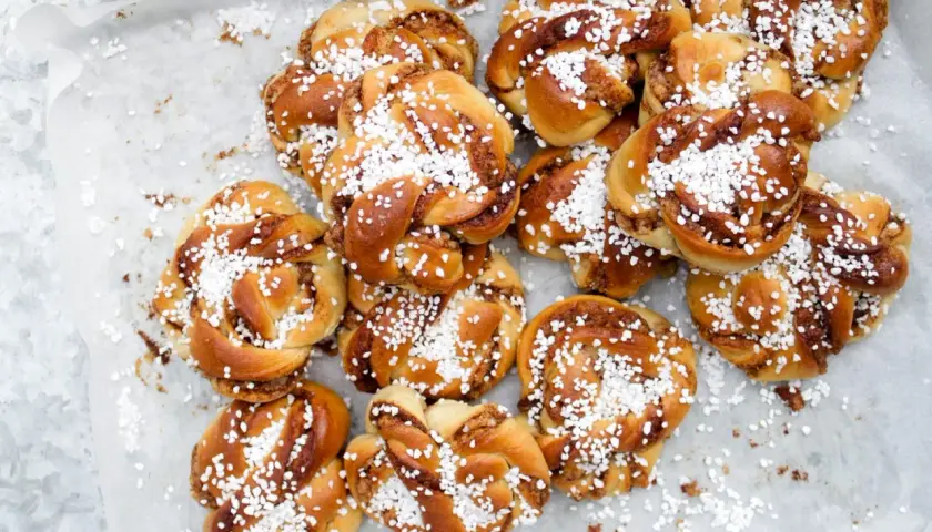 En hög med gyllene kanelbullar, toppade med pärlsocker. Perfekt för en fika, dessa sukat frukt-inspirerade bakverk doftar ljuvligt.