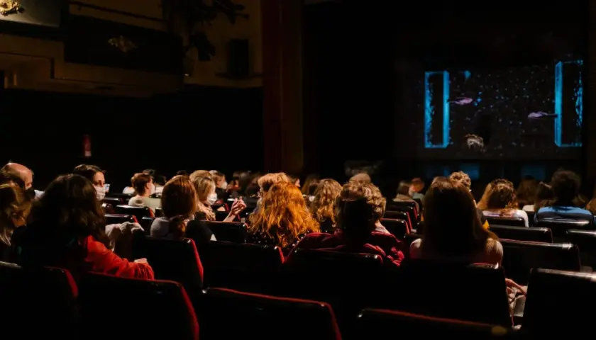 Pubblico in sala, immerso nell'oscurità, attende con il fiato sospeso i monologhi da brividi che stanno per iniziare sul palco illuminato.