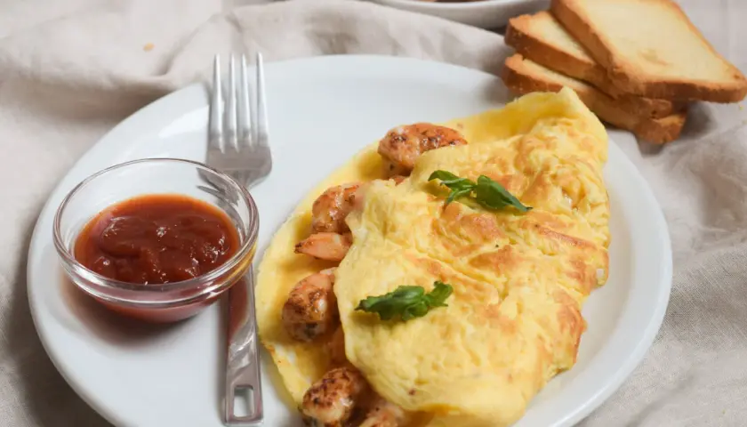 Tortilla de gambas dorada y jugosa, servida con salsa y tostadas. Un desayuno perfecto.