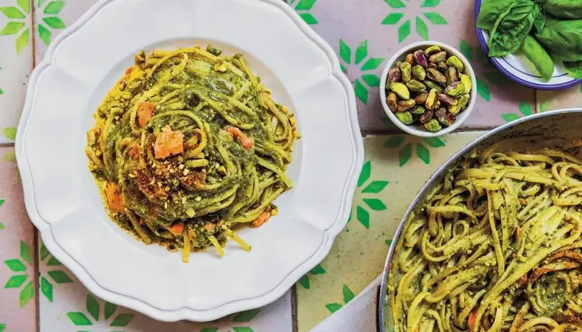 Pyszne linguine z zielonym pesto i kawałkami łososia, posypane pistacjami. Różnorodne kształty makaronu tworzą apetyczną całość.