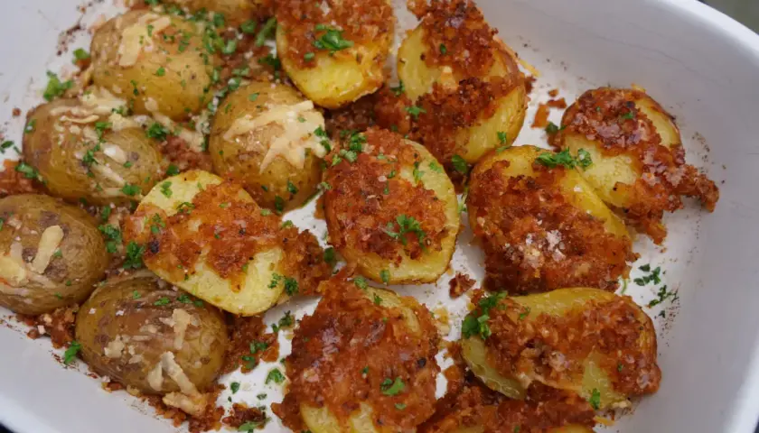 Knusprige parmesan kartoffeln mit Petersilie und grobem Salz bestreut, bereit zum Genießen.
