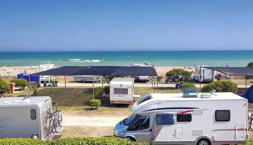 Autocaravanas y caravanas en un camping junto al mar, ideal para camping en Barcelona. El mar azul y la playa invitan a disfrutar del sol.