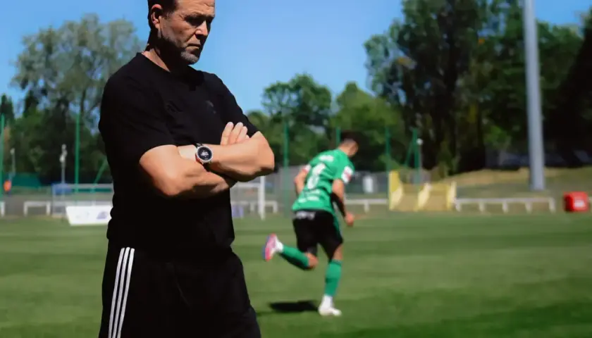 Trener Górnika Łęczna z rękami skrzyżowanymi na piersi obserwuje trening.