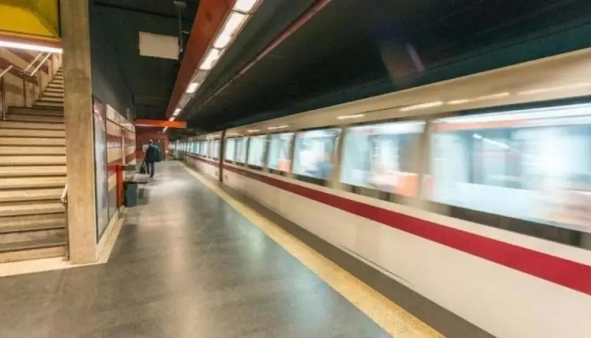 Treno in corsa su binari di una stazione metro. Si intravedono scale e un passeggero in attesa. Le fermate metro a Chiuse sono un luogo di passaggio frenetico.