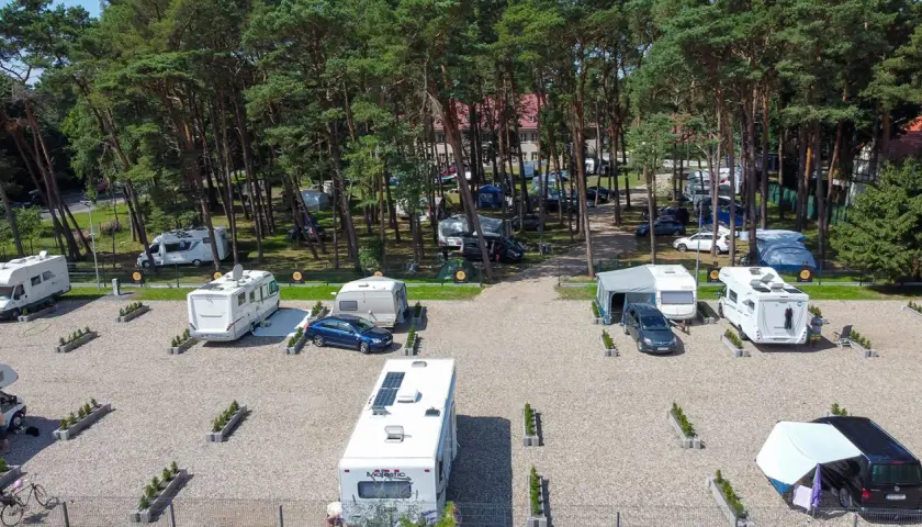 Kampery i przyczepy kempingowe na żwirowym polu namiotowym w lesie sosnowym. Widok z lotu ptaka na sea camp Rogowo.