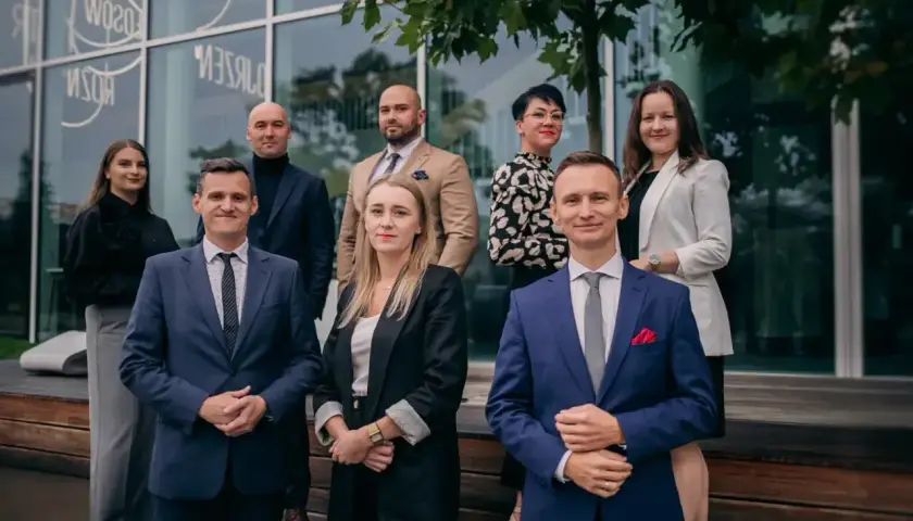 Grupa prawników w eleganckich strojach pozuje przed nowoczesnym budynkiem.