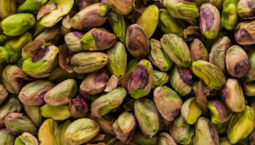 Zbliżenie na stos łuskanych pistacji, niektóre z zielonymi nasionami, inne z brązowymi łupinami.