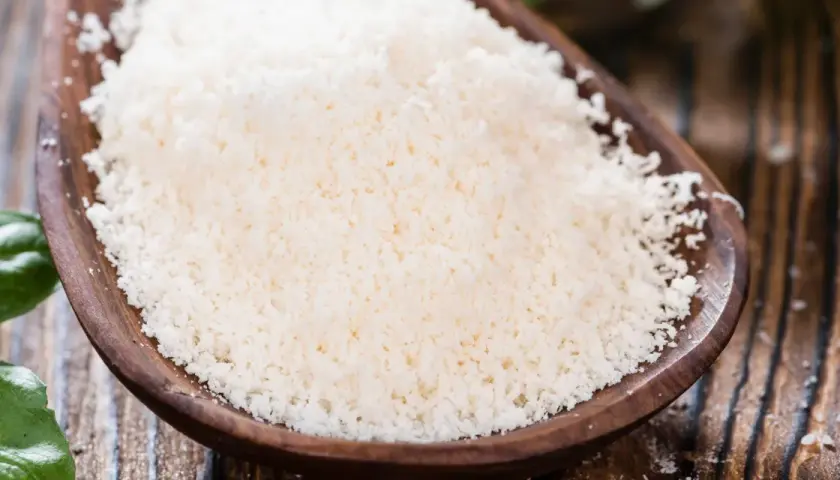 Cuchara de madera con rallado fino de parmesano vegano, listo para espolvorear sobre tu plato favorito.