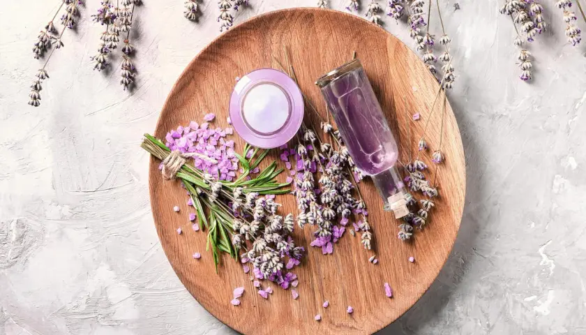Sur un plateau en bois, des brins de lavande fraîche et séchée, des cristaux violets et une petite bouteille de liquide pour faire bouillir de la lavande.